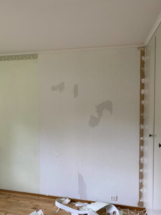 Vägg under renovering med delvis bortriven tapet och tapetavfall på golvet.