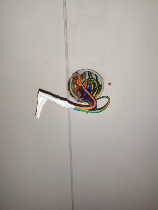 Öppen takdosa med oskyddade elektriska kablar och anslutningar, tejpade kablar hänger från taket.