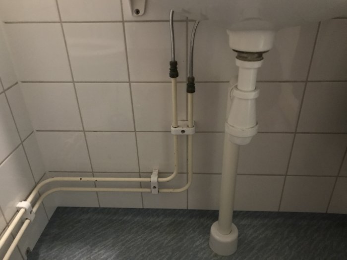Synliga rör och avloppsstam i ett hörn av ett badrum, potentiell utmaning för dold installation.