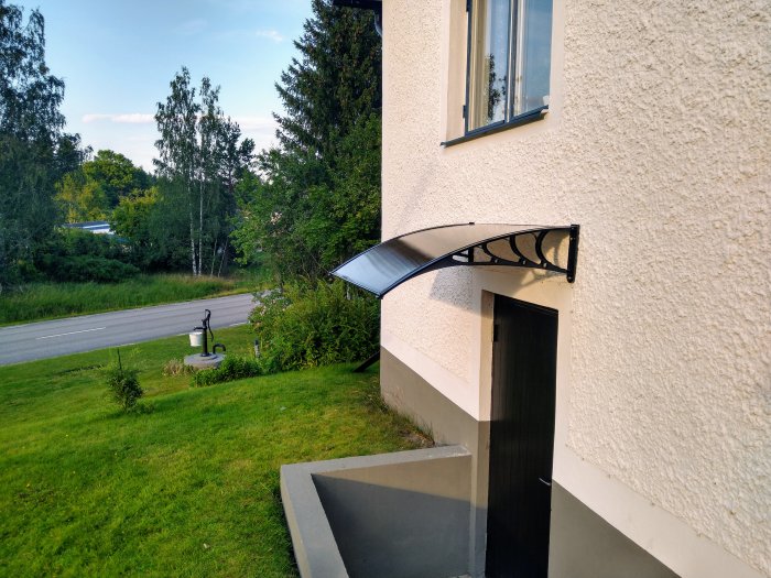 Nyinstallerat genomskinligt tak ovanför en källardörr på ett hus, med svarta stödbågar.