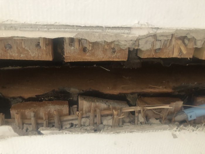 Hål i taket där gammal vägg har tagits bort, visar puts, vass, ståltråd och underliggande planktak.