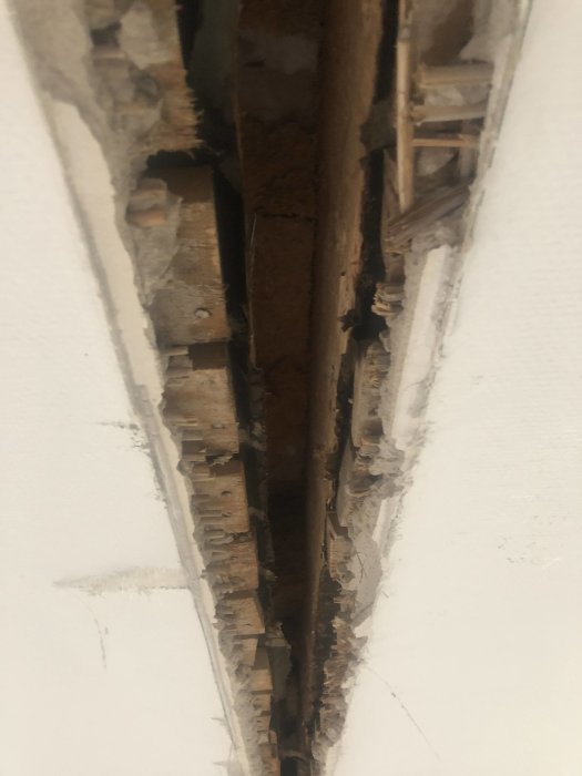 Hål i taket där en vägg tagits bort, visar synliga plankor och trasig kant där puts möter vävtapet.