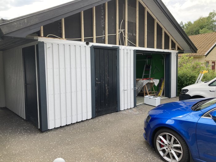 Garage med nyuppsatt stående vit panel och pågående arbetsområde inuti, med byggmaterial synligt.