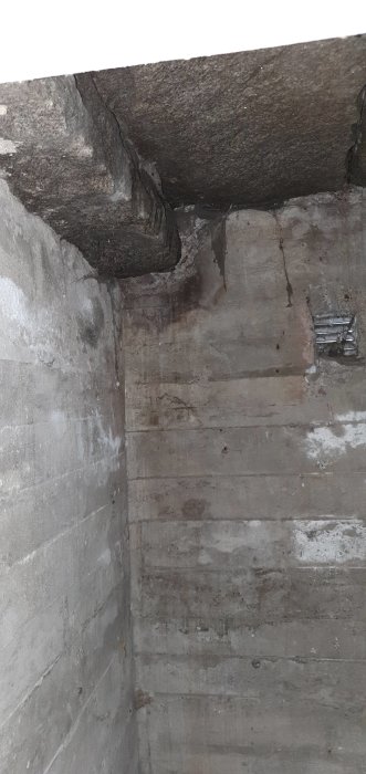 Ofärdigt isoleringsarbete i ett litet rum under entrétrappan med synlig betongvägg och delvis påbörjad isolering med plast och glasull.
