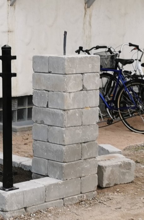 Nybyggd murstolpe för grind med utstickande armeringsjärn, intill parkerade cyklar.