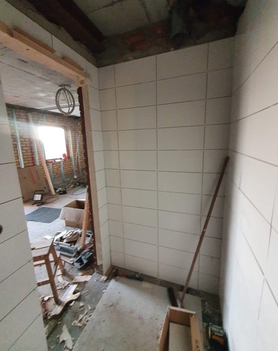 Renoveringsprojekt med nyligen kaklade väggar i ett rum under ombyggnad, byggmaterial och verktyg synliga.