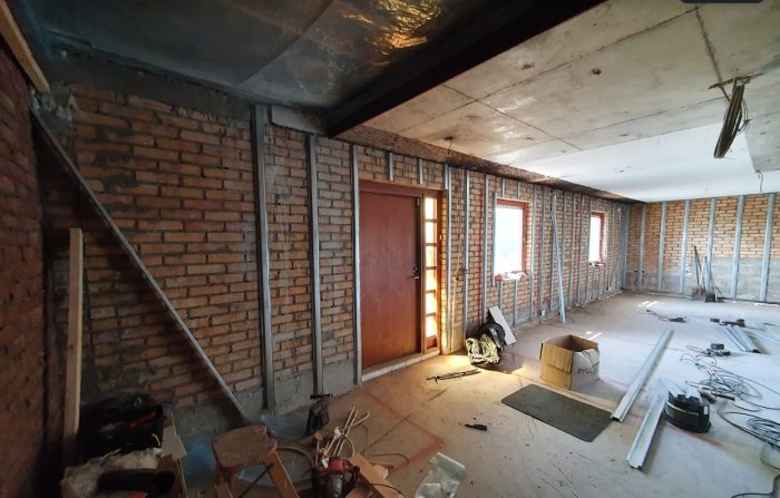 Renoveringsarbete i ett tomt rum med tegelväggar, synliga plåtreglar och oavslutat innertak.