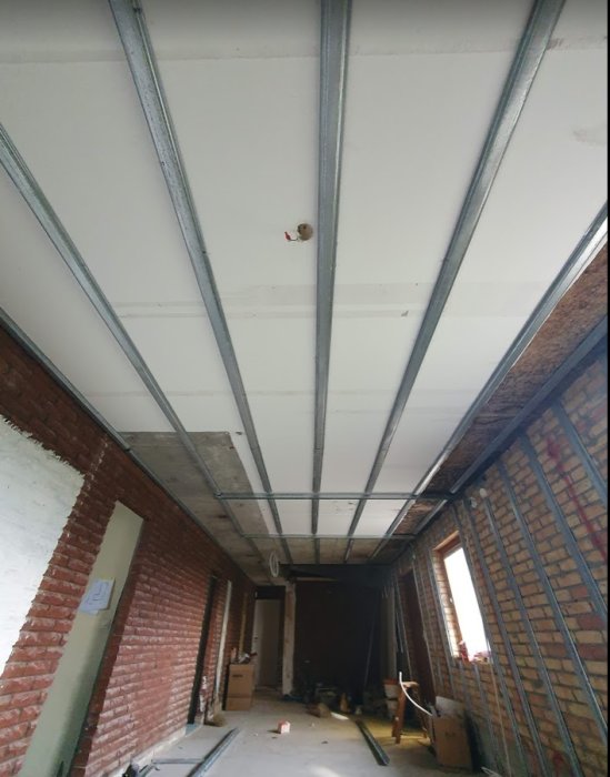 Renoveringsprojekt med nya metallreglar monterade i taket i ett ofärdigt rum med tegelväggar.