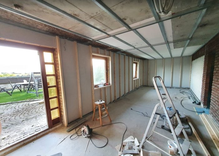 Renoveringsfas av ett hem med exponerade isolerade väggstolpar och omonterat innertak med synliga plåtprofiler.