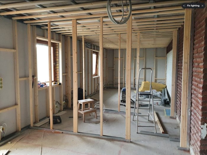 Ett pågående byggprojekt med exponerade träreglar och stege i ett orenoverat rum.