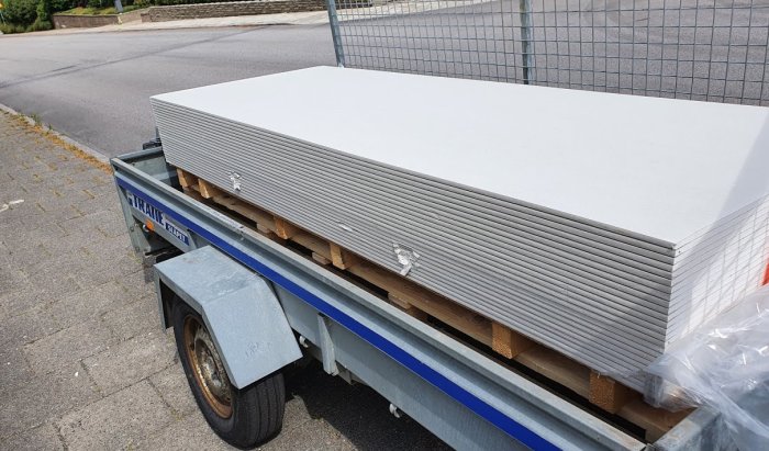 Släpvagn lastad med staplar av vita fibercementskivor redo för installation i renoveringsprojekt.