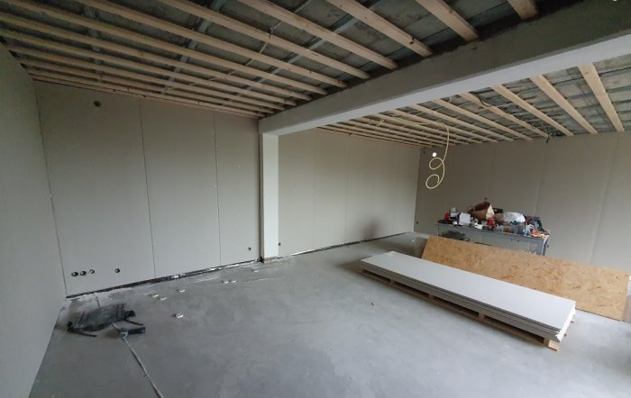 Renoveringsarbete i rum med oskyddade fibercementskivor på väggar, träreglar i taket och byggmaterial på golvet.