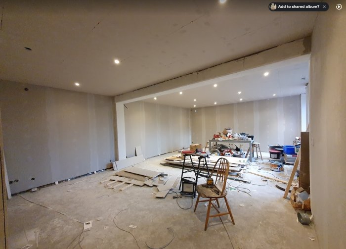 Renoveringsrum med gipsade väggar och tak, spotlights installerade, och byggmaterial på golvet.