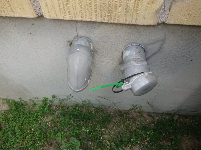 Två gamla plomberade oljerör som sticker ut från en husvägg.