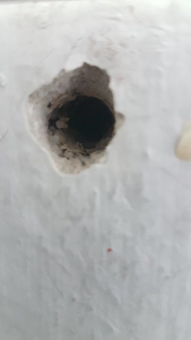 Förstorat hål i ett poröst vitt tak där ett gardinfäste lossnat.