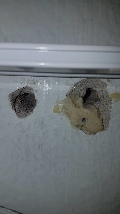Två hål i vit vägg, det högra delvis fyllt med otillräckligt fixmaterial.