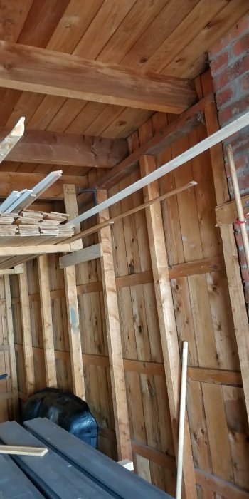 Interiör av garage med träpanel och takbjälkar, synligt regelverk och isoleringsmaterial.