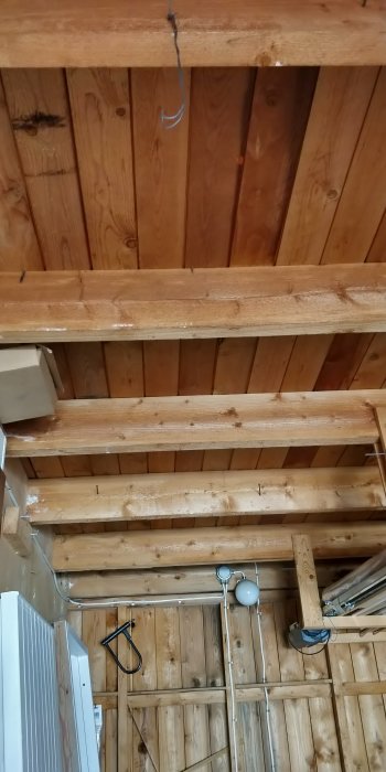 Träbjälkar och väggpanel i ett garage som förbereds för isolering med synlig vindduk och luftspalt.