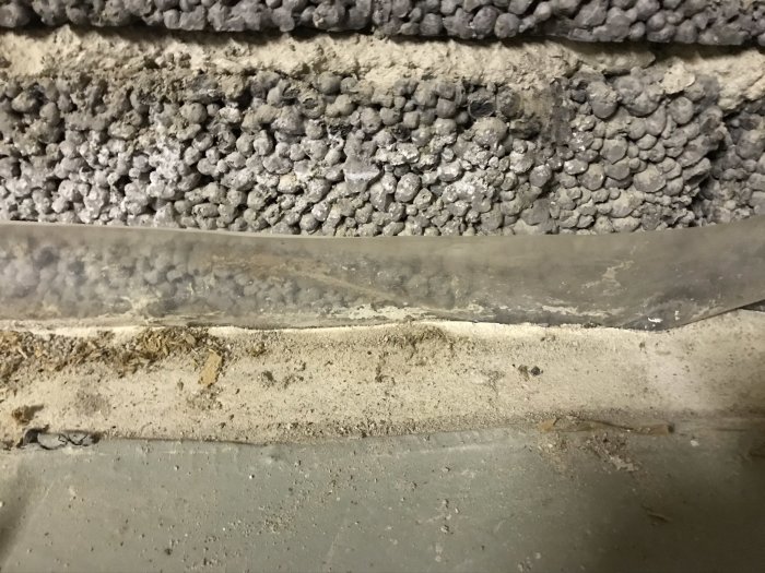 Betonggolv med grå färgrester längs kanter, framför en vägg med lätta kullerstensliknande konstruktioner.