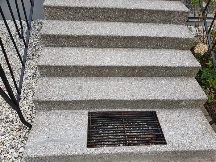 Äldre entretrappa med grått krossad stenmönster och metallräcke, undrar över ytbeläggningen.