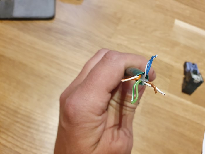 Hand håller en uppsprättad nätverkskabel med färgkodade trådar som korsar varandra.