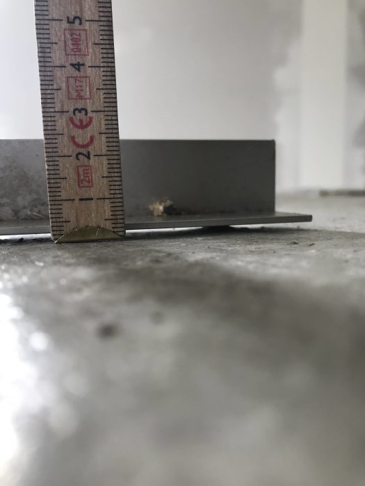 Mätsticka visar ojämn höjdskillnad på en nygjuten betongplatta som är knottrig och har sprickor.