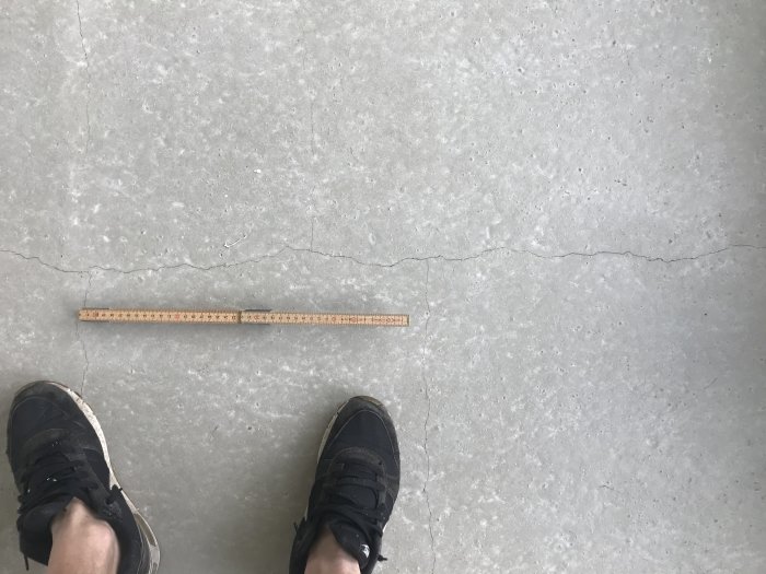 Knottrig betongplatta med sprickor bredvid linjal och en persons fötter som indikerar måttet på ojämnheten.