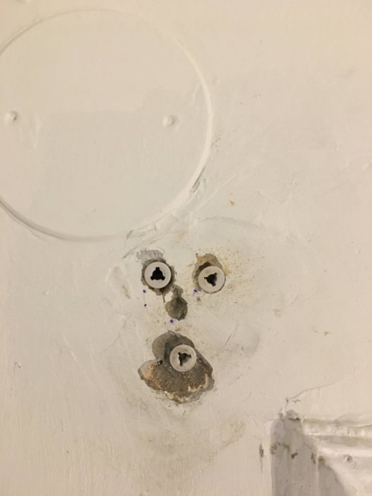 Plastpluggar gjutna i ankarmassa på vit vägg, i väntan på att fästa skruvar och hållare.