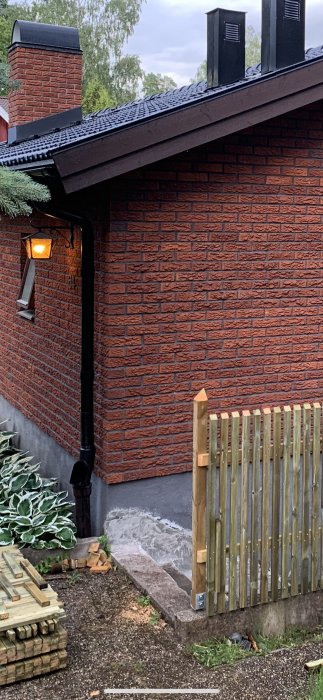 En del av rödtegelhus med ett påbörjat trästaket vid en trappa som leder ner till en källare.