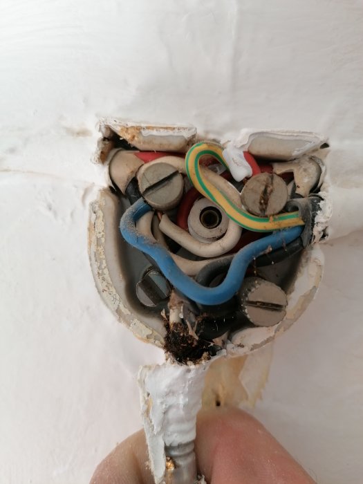 Öppen gammal porslinsdosa med synliga elledningar och färgade kablar i en vägg.