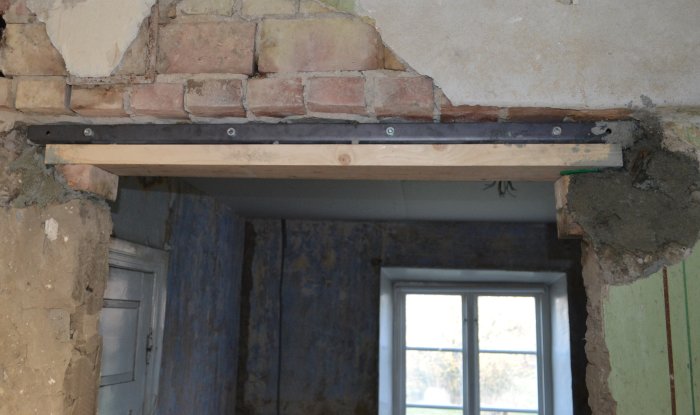L-järn och gängstång stödjer ett valv ovanför en gammal dörröppning under renovering.