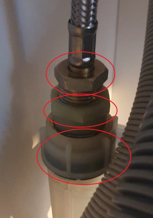 Närbild på tre muttrar för anslutning av köksblandarslangar och diskmaskinslang markerade med röda cirklar.