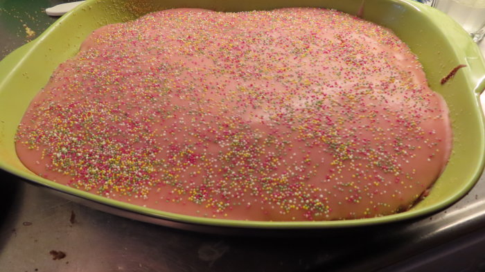 Citronsockerkaka med rosa jordgubb/citron-frosting och färgglada strössel i bakform.
