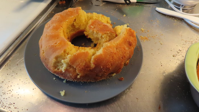 Citronsockerkaka på ett fat med bitar urtaget, smulor runt om, på en köksbänk.