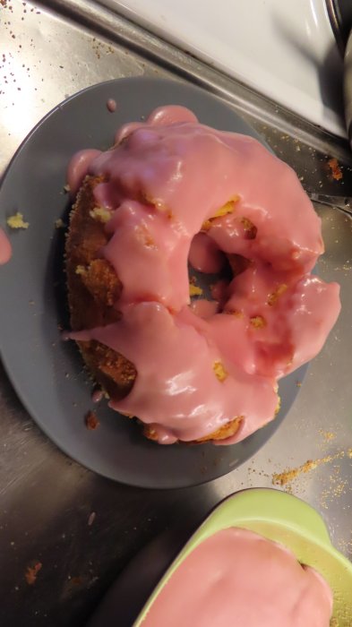 Citronsockerkaka med rosa jordgubb/citron-frosting på ett blått fat, överbliven frosting i skål.