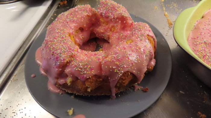 En saftig citronsockerkaka med rosa jordgubb-citronfrosting och strössel på ett mörkt fat.
