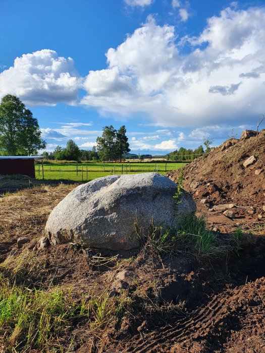 Stor sten i jordig terräng, svår att flytta, med gräs och himmel i bakgrunden.