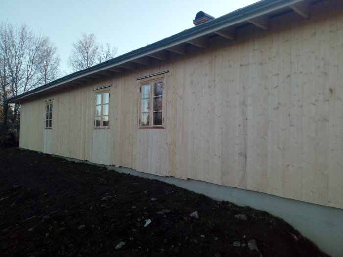 Nyinstallerade fönster och dubbeldörr i en fasad med ljusa träpaneler på ett hus under renovering.