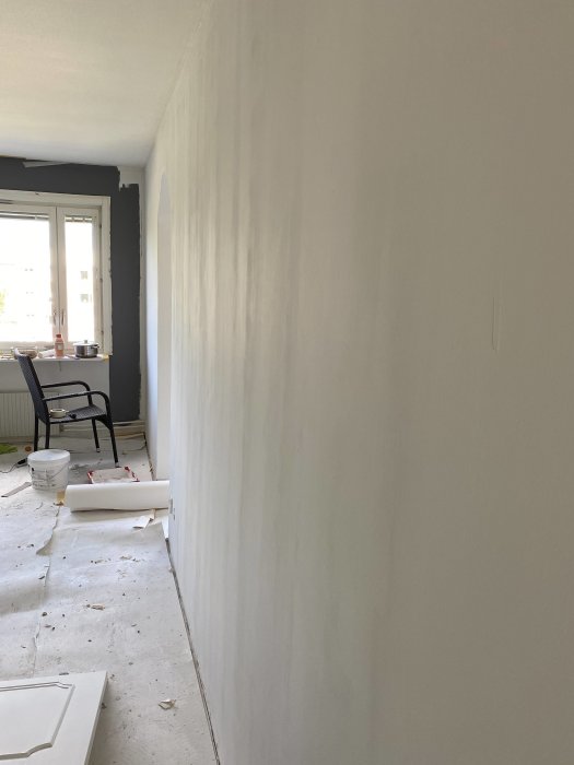 Nymålat rum med synliga linjer på väggen efter spackling och slipning, med målartillbehör i bakgrunden.