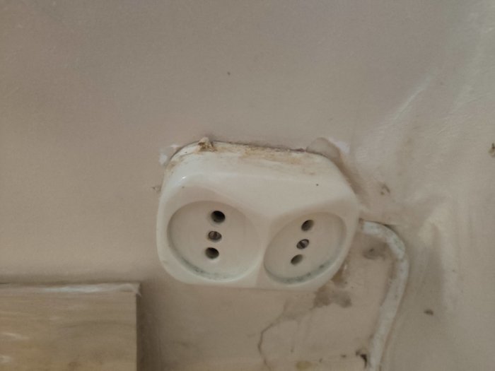 Gammal sliten vägguttag på en smutsig vägg, möjlig indikation på äldre elinstallation.
