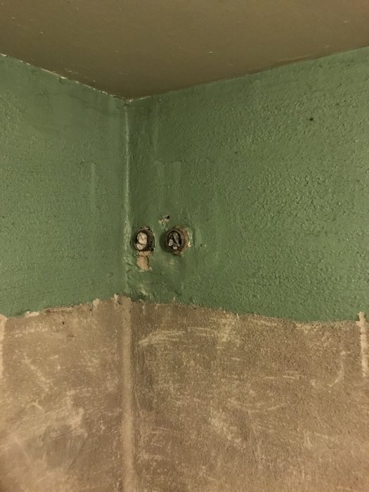 Vägghörn där rörinstallationer är inborrade och delvis kapade med synliga märken i sockelputsen.