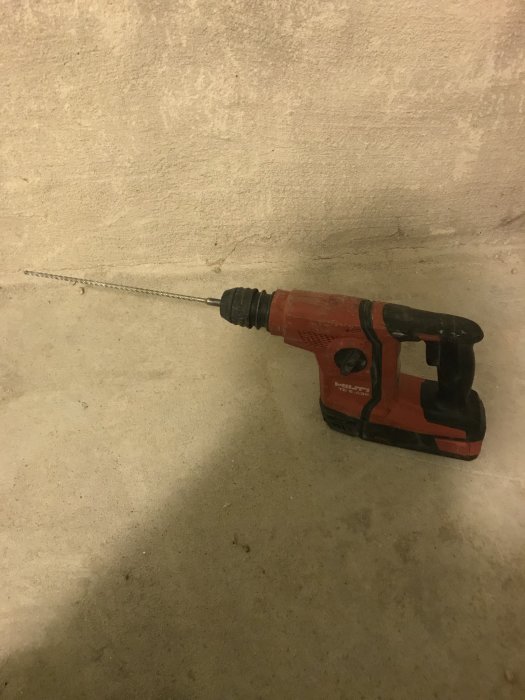 Röd borrmaskin med långt borrstål mot en betongvägg efter arbete med rörinstallation.