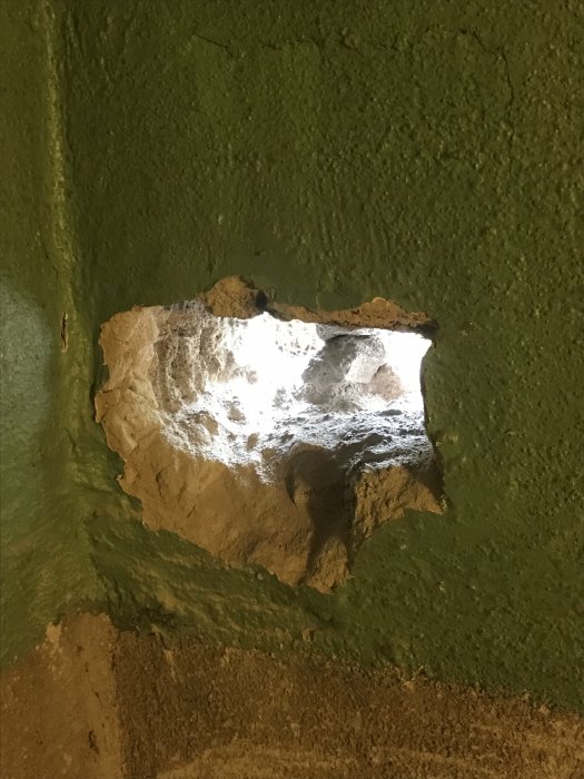 Hål i grön sockelputs där rör böjs och kapats för installation, med synlig inre struktur och kant.