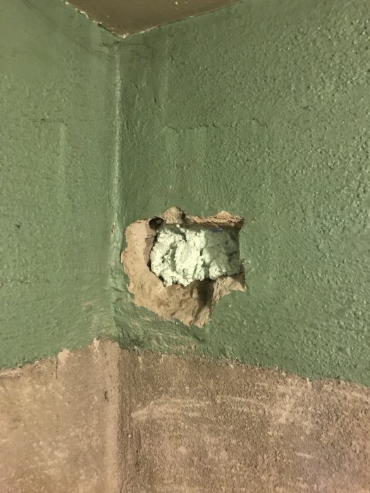 Hål i en sockelputsad vägg med synliga rörrester och fogskum, skadat under arbete.