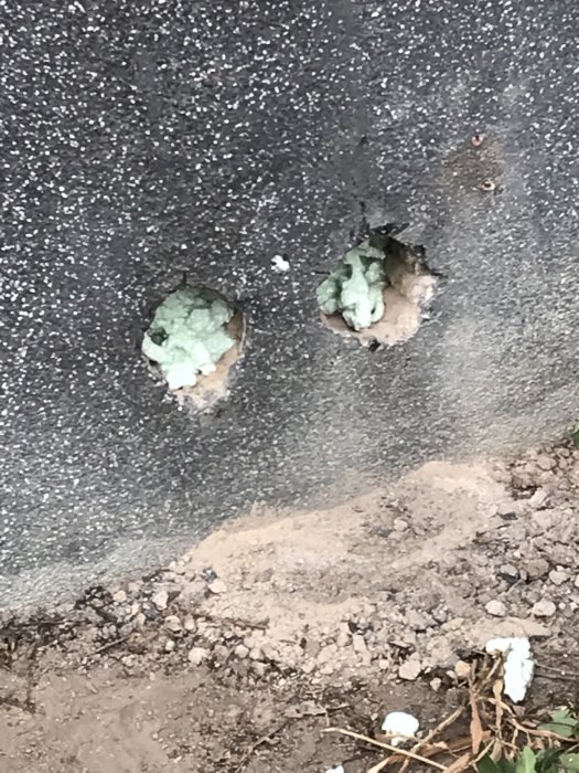 Hål i sockelputs med rester av fogskum runt rörgenomföringar efter kapning.