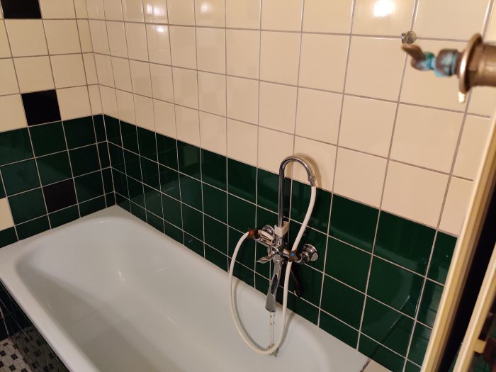 Retro badkar med beige och gröna kakelplattor samt gammaldags kran.