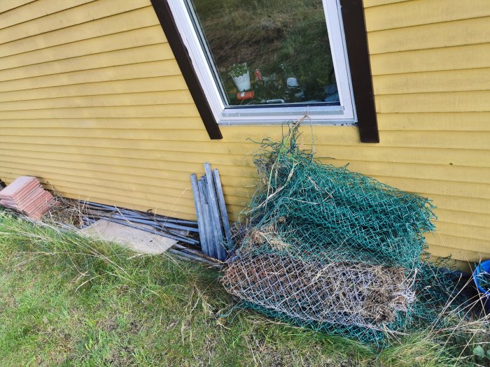 Metallstängsel och skrot ligger i en hög vid en gul vägg bredvid husets fönster.