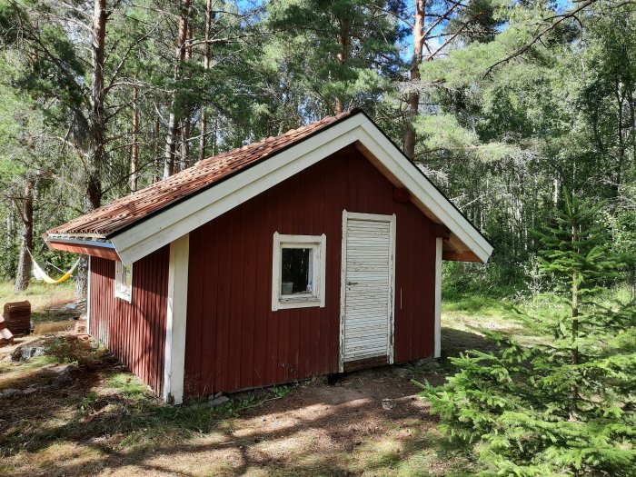 Röd stuga med ny vindskiveplåt och nockpannor omgiven av skog.