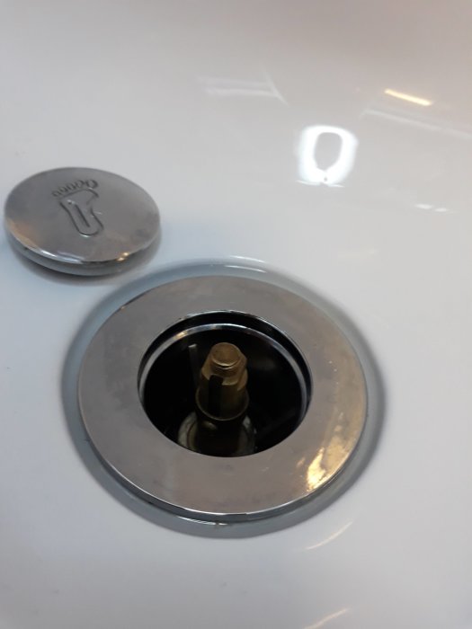 Avlopp med öppet lock i en duschkabin, mynt för storleksjämförelse.