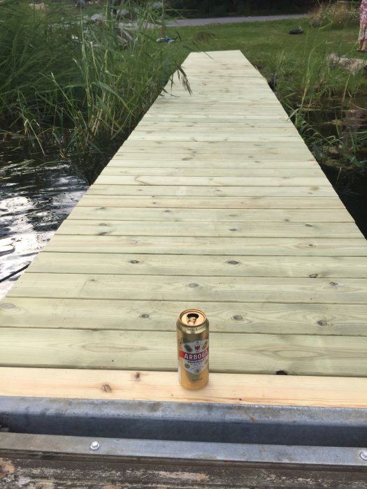 Nya trälandgångar på en flotte med en ölburk uppställd i förgrunden som belastningstest, vid en sjöstrand.